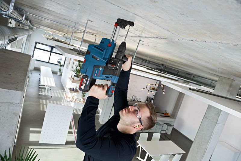 En person iført sikkerhedsudstyr borer ind i et betonloft i et moderne arbejdsområde.