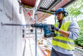 En person iført sikkerhedsudstyr borer i beton med en batteridrevet borehammer.