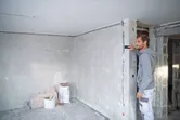 En person måler en væg med en lasermåler i et delvist færdigt rum.