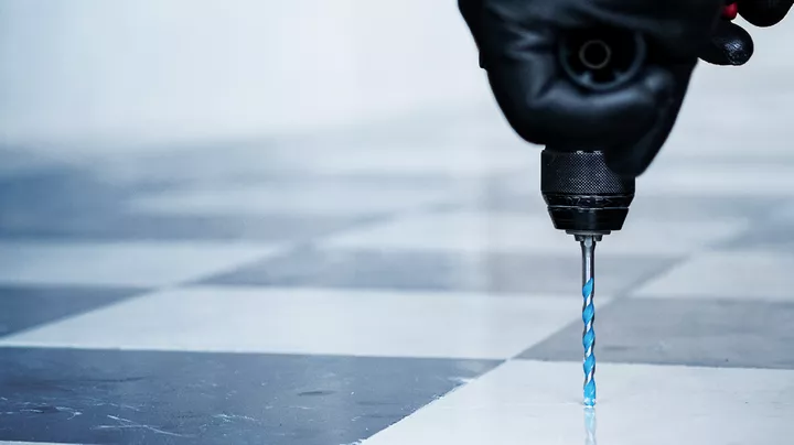 En person iført sikkerhedsudstyr borer i et flisebelagt gulv.