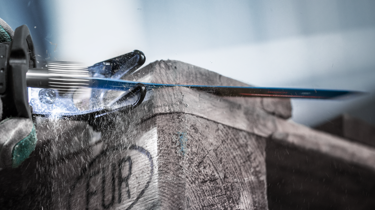 En person iført sikkerhedsudstyr bruger en bajonetsav til at skære igennem en trækasse.