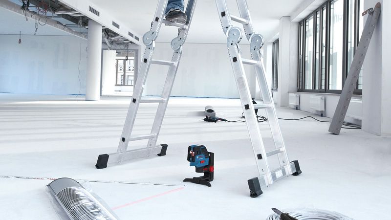 Et lasernivelleringsværktøj projicerer røde linjer på gulvet i et lyst, ufærdigt rum.