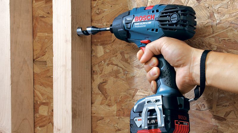 En person bruger en batteridrevet slagnøgle til at bore i en træramme.