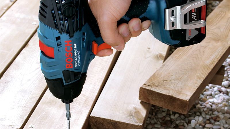 En person bruger en batteridrevet slagnøgle til at skru en skrue i træplanker.