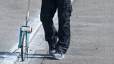 En person iført sikkerhedsudstyr måler vejafstand med et målehjul.