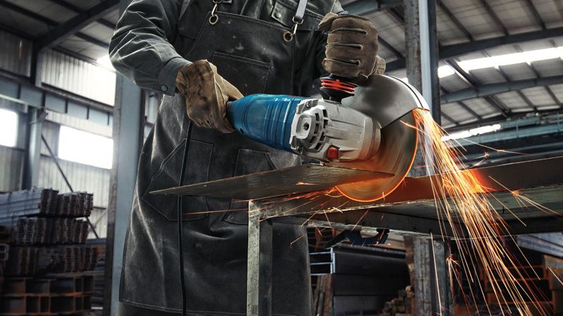 En person iført sikkerhedsudstyr skærer metalplader med en stor vinkelsliber, hvorved der flyver gnister.