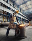 En arbejder iført sikkerhedsudstyr sliber metal med en stor vinkelsliber på en fabrik.