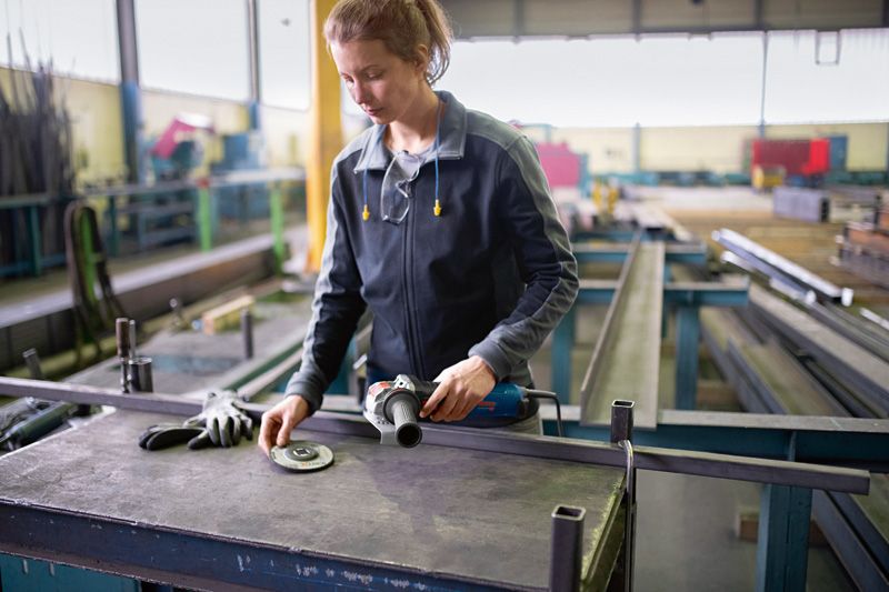 En person iført sikkerhedsudstyr forbereder en vinkelsliber på en metalbænk.