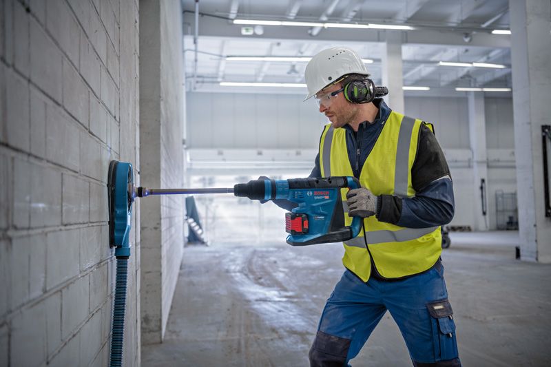 En person iført sikkerhedsudstyr borer ind i en betonvæg med en batteridrevet borehammer.