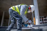 En person iført sikkerhedsudstyr bruger en batteridrevet vinkelsliber til at skære en betonplade.