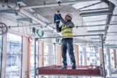 En person iført sikkerhedsudstyr borer i et betonloft på en byggeplads.