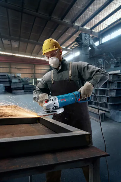 En person iført sikkerhedsudstyr sliber metal og skaber gnister på en fabrik.