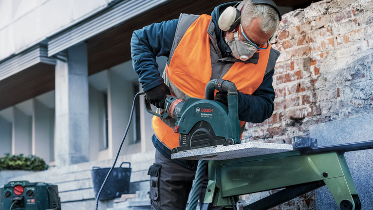 En person iført sikkerhedsudstyr saver sten med en rundsav på en arbejdsbænk.