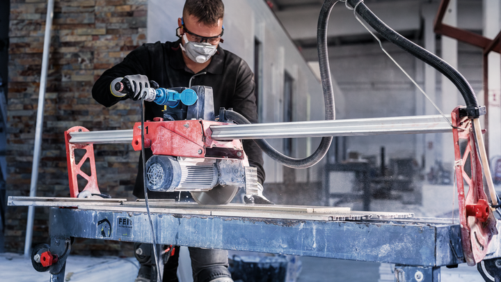 En person iført sikkerhedsudstyr betjener en flisesav i et industrielt miljø.