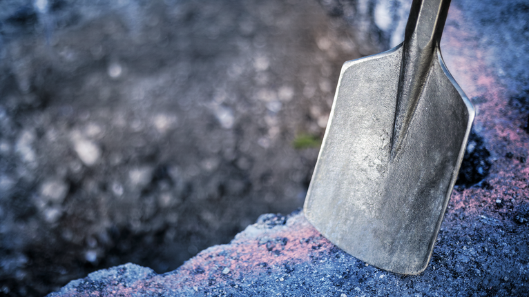 Skovlblad hviler på ru beton ved kanten af et gravet hul.