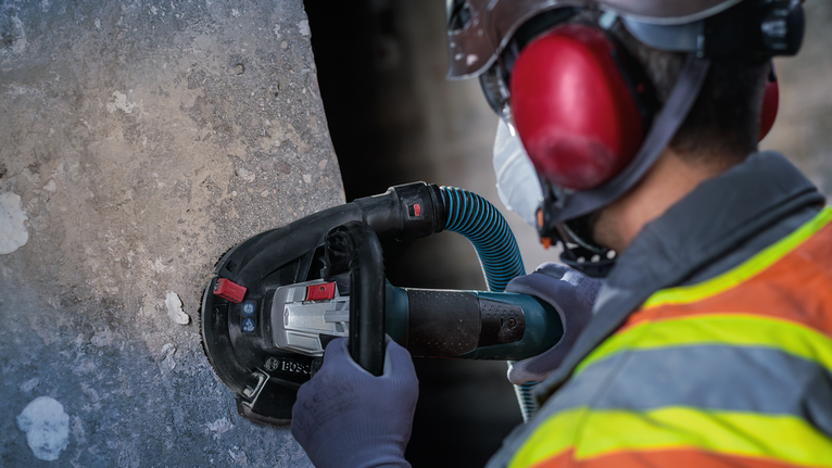 Arbejder iført sikkerhedsudstyr polerer beton med en håndholdt elektrisk sliber.