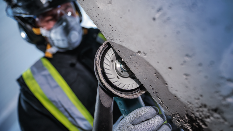 En person med sikkerhedsudstyr sliber beton med et håndholdt elværktøj.
