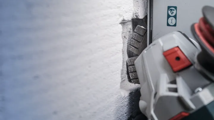 Murfræser skærer en lige rille i en betonvæg.