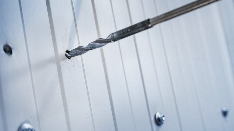 Borehoved laver et hul i et hvidt metalpanel.