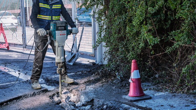 En person iført sikkerhedsudstyr bryder beton ned med en nedrivningshammer.