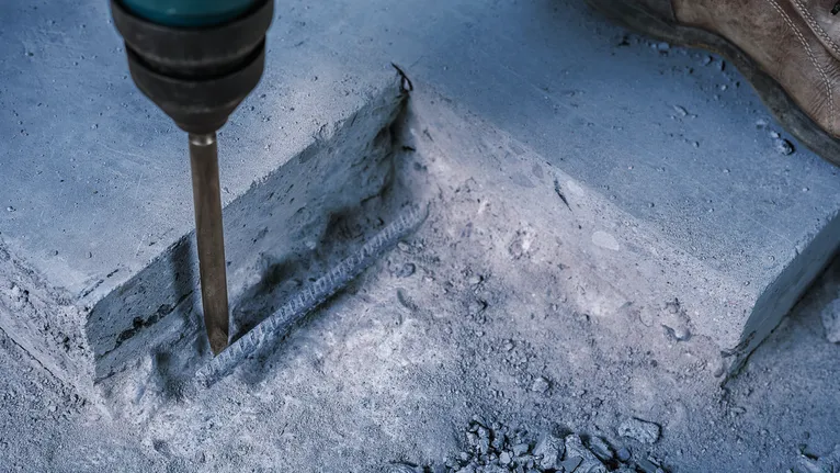 Person iført sikkerhedsudstyr bryder beton med en mekanisk mejsel.