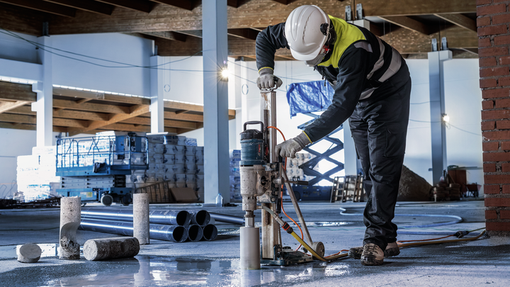 En person iført sikkerhedsudstyr borer i beton på en byggeplads.