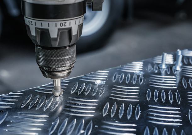 En boremaskine strammer en bolt ind i en tekstureret metalplade.