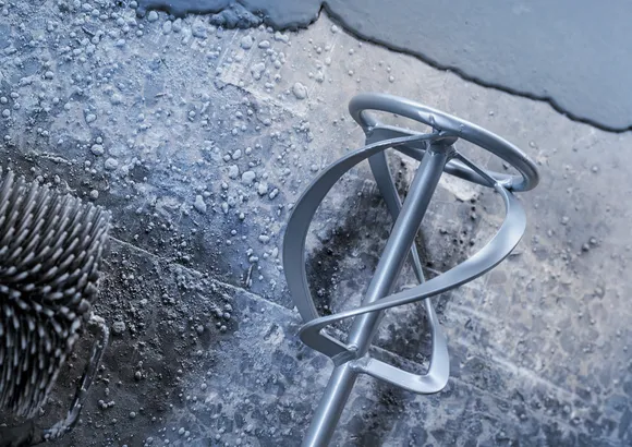Malingsblanderpaddel hviler på en struktureret overflade med våd beton.