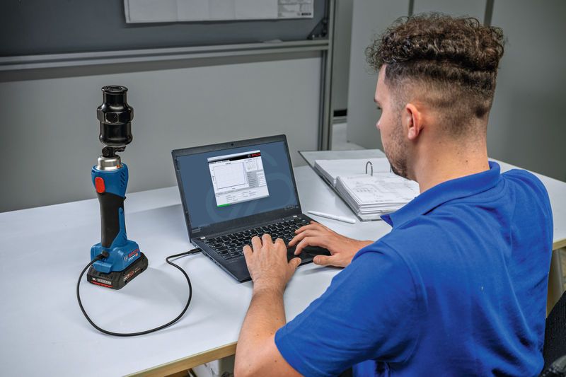 En person forbinder et batteridrevet hydraulisk stanseværktøj til en bærbar computer ved et skrivebord.