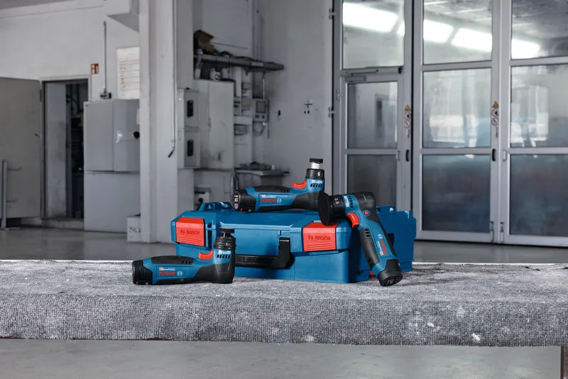 Batteridrevne excenterslibere og en blå kasse placeret på en betonoverflade i et værksted.