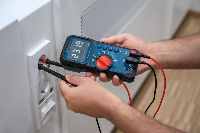 En person tester en stikkontakt i væggen med et digitalt multimeter.