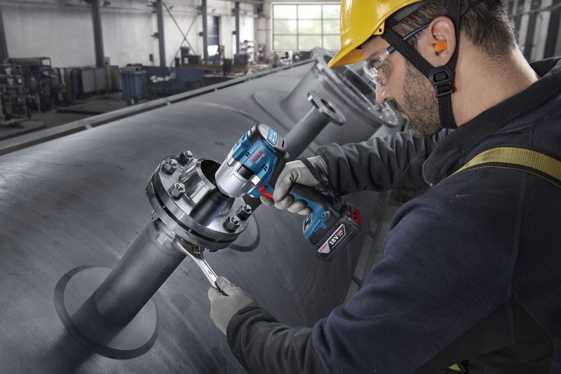 En person iført sikkerhedsudstyr strammer bolte på industrielle rør med en batteridrevet slagnøgle.