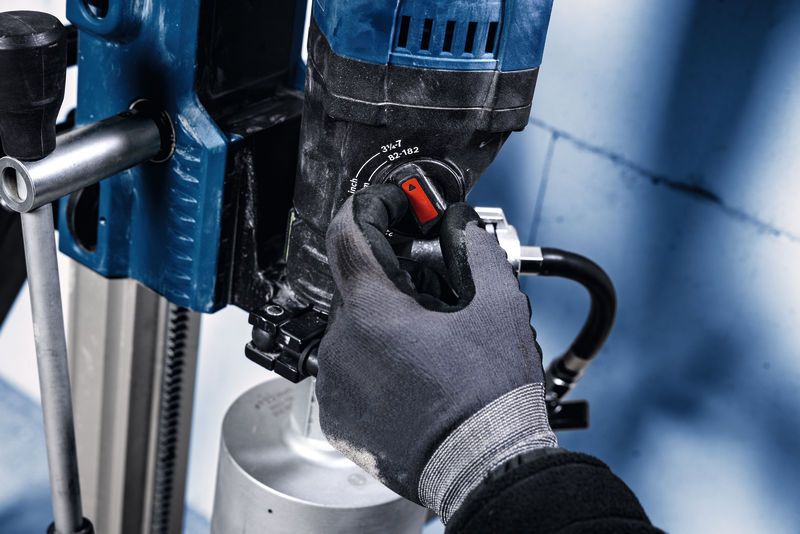 En person med sikkerhedsudstyr justerer en drejeknap på en monteret diamantboremaskine.