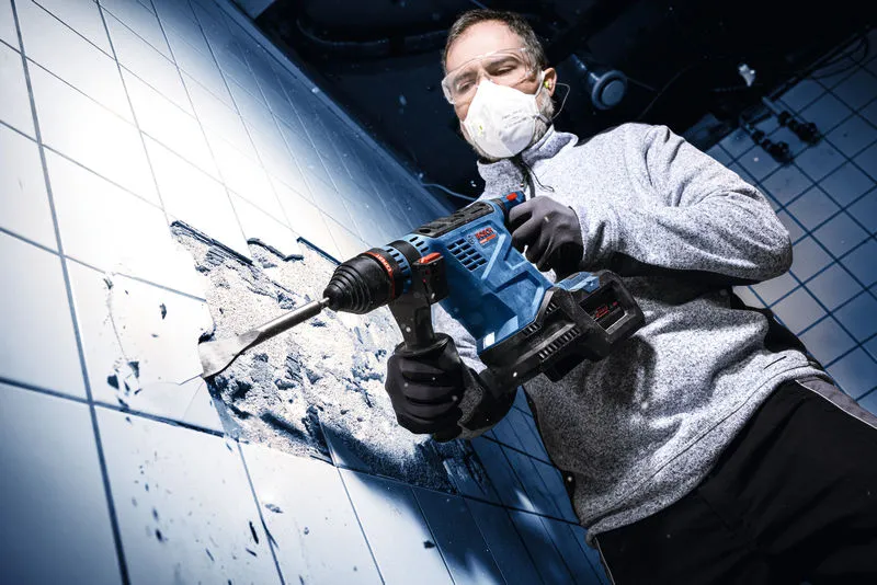 En person iført sikkerhedsudstyr borer i en flisebelagt væg med en batteridrevet borehammer.