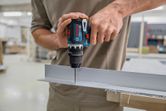 Person, der bruger en batteridrevet boremaskine til at lave et hul i en metalkanal.