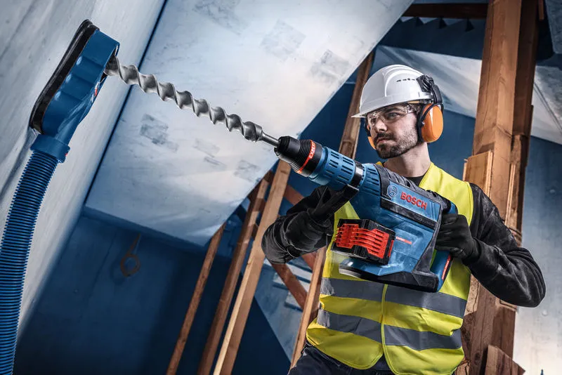 En person iført sikkerhedsudstyr borer i beton med en batteridrevet borehammer.