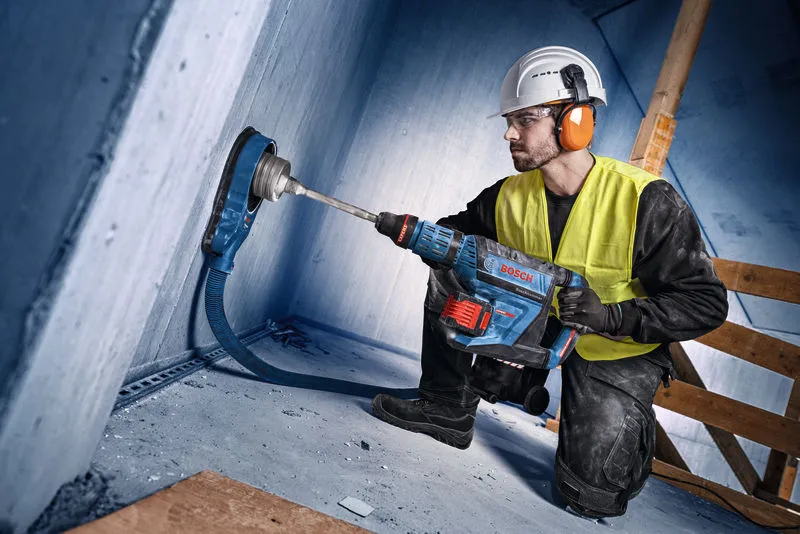 En person iført sikkerhedsudstyr borer ind i en betonvæg med en stor borehammer.