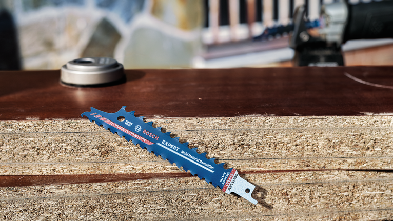 Savbladet hviler på en stak træpaneler udendørs.