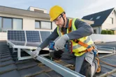 En person iført sikkerhedsudstyr installerer en solpanelramme med en batteridrevet slagboremaskine.