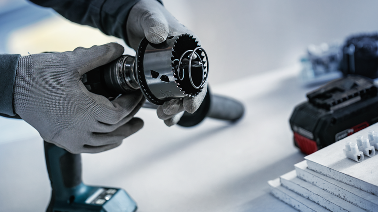 En person med sikkerhedsudstyr fastgør en hulsav til en batteridrevet boremaskine.