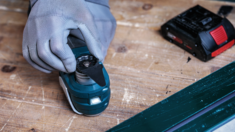 En person med sikkerhedsudstyr fastgør en klinge til et elværktøj på en arbejdsbænk.