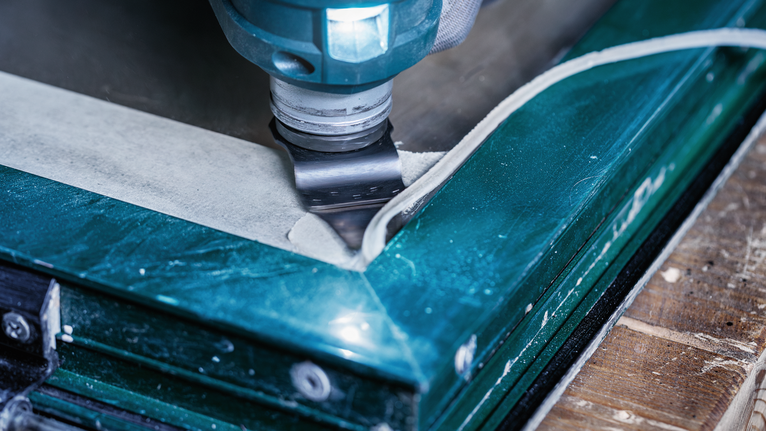 Oscillerende værktøj, der skærer igennem en fugemasse til vinduesrammer.