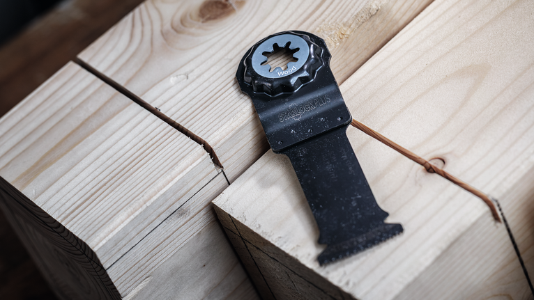 Oscillerende savklinge placeret på træbjælker med et præcist snit og en styretråd.