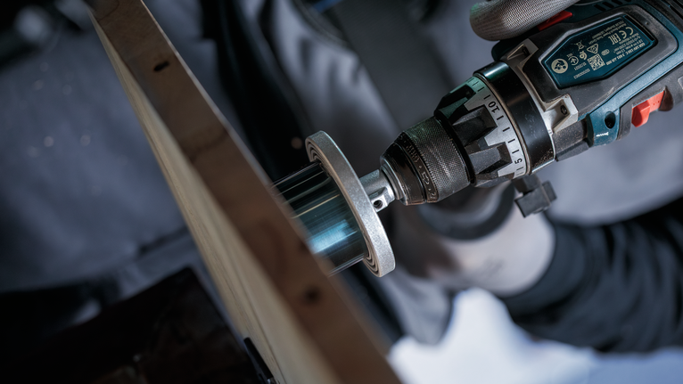 Person iført sikkerhedsudstyr bruger en boremaskine med en hulsav på træ.