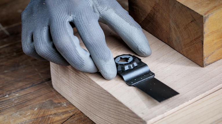En person med sikkerhedsudstyr fastgør et metalsavklinge til en træoverflade.