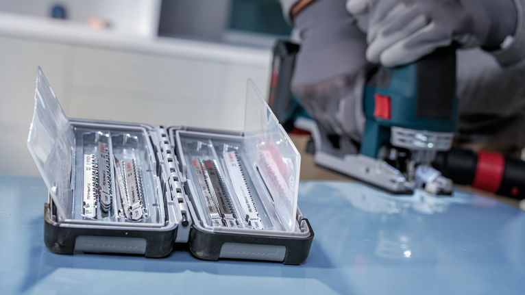 En person med sikkerhedsudstyr bruger en stiksav nær en åben kasse med savklinger.