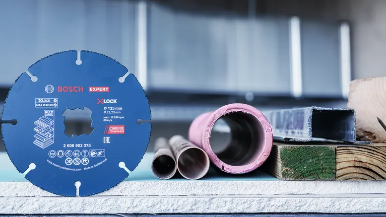 Rundsavklinge vist oprejst ved siden af metalrør og byggematerialer.