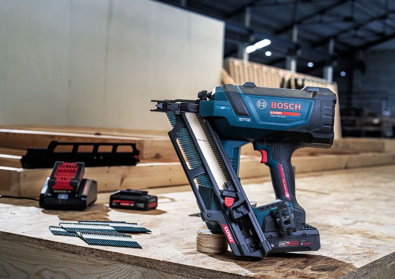 Batteridrevet sømpistol med søm, batterier og oplader på en træarbejdsbænk.
