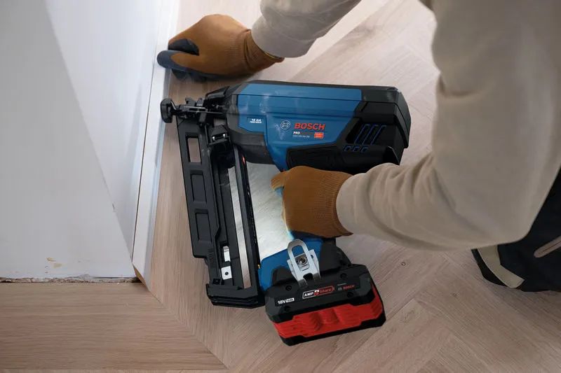 En person iført sikkerhedsudstyr bruger en batteridrevet sømpistol på gulvlister.