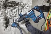 En person iført sikkerhedsudstyr bruger en borehammer til at bore i beton.
